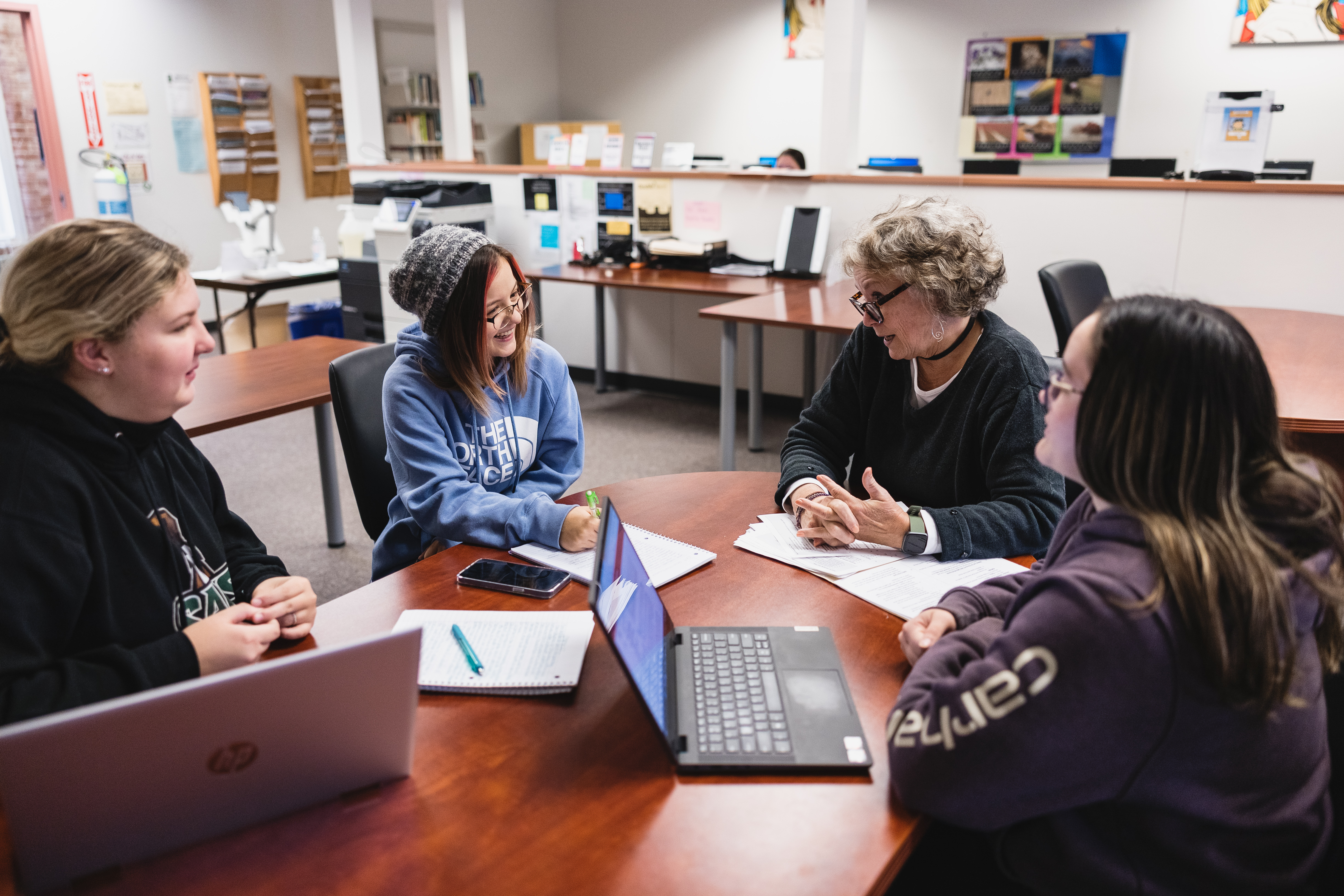 Students sit at a table with an instructor in a classroom