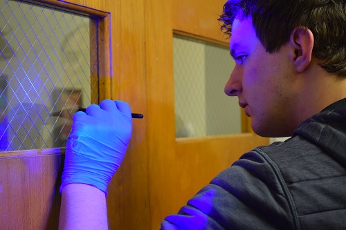A criminal justice student taking a fingerprint off off a door.