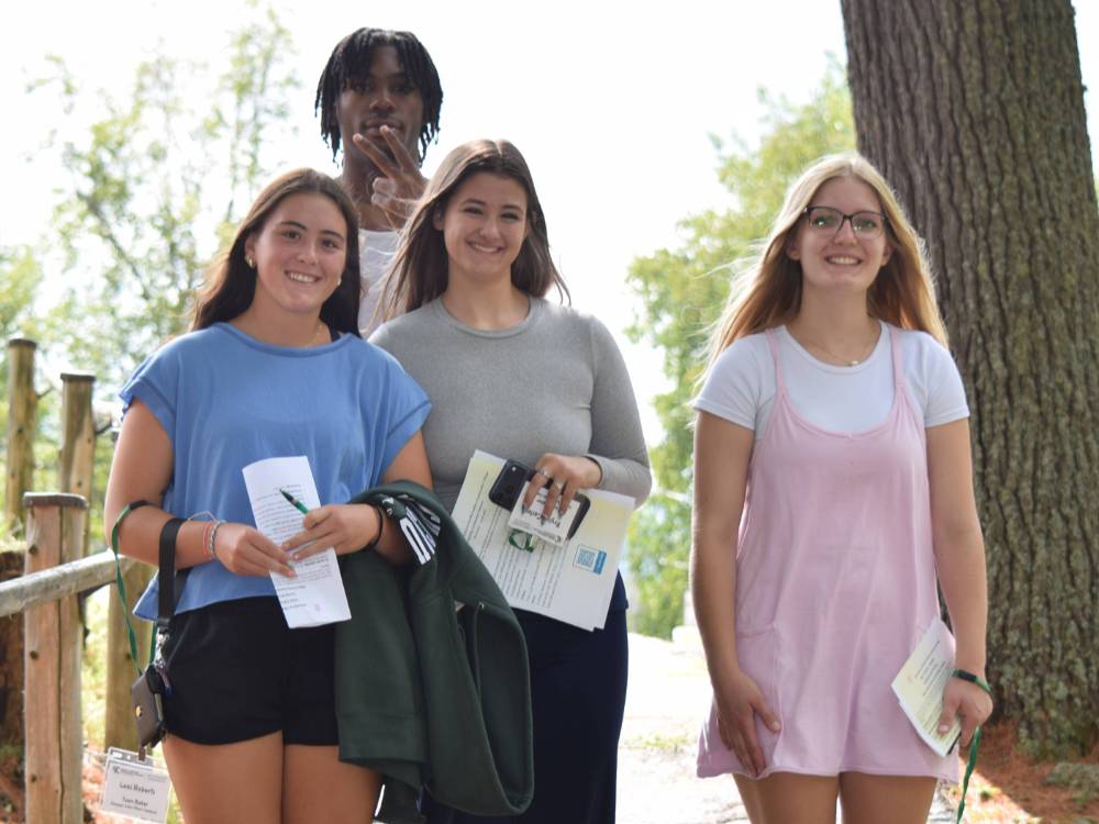 A group of four college students stand on a pathway and smile for the camera.