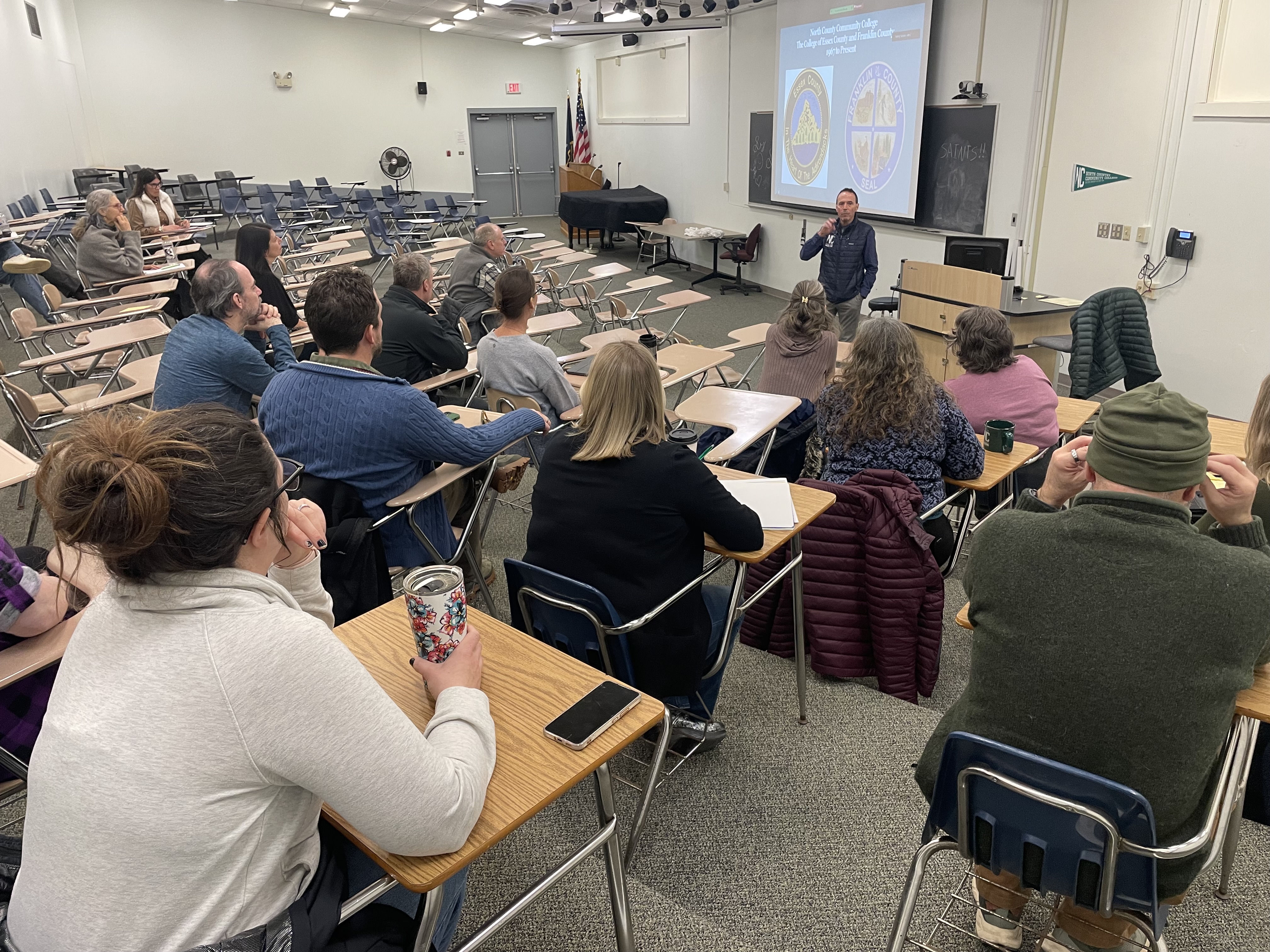Employees sit in a lecture hall listening to the college president speak