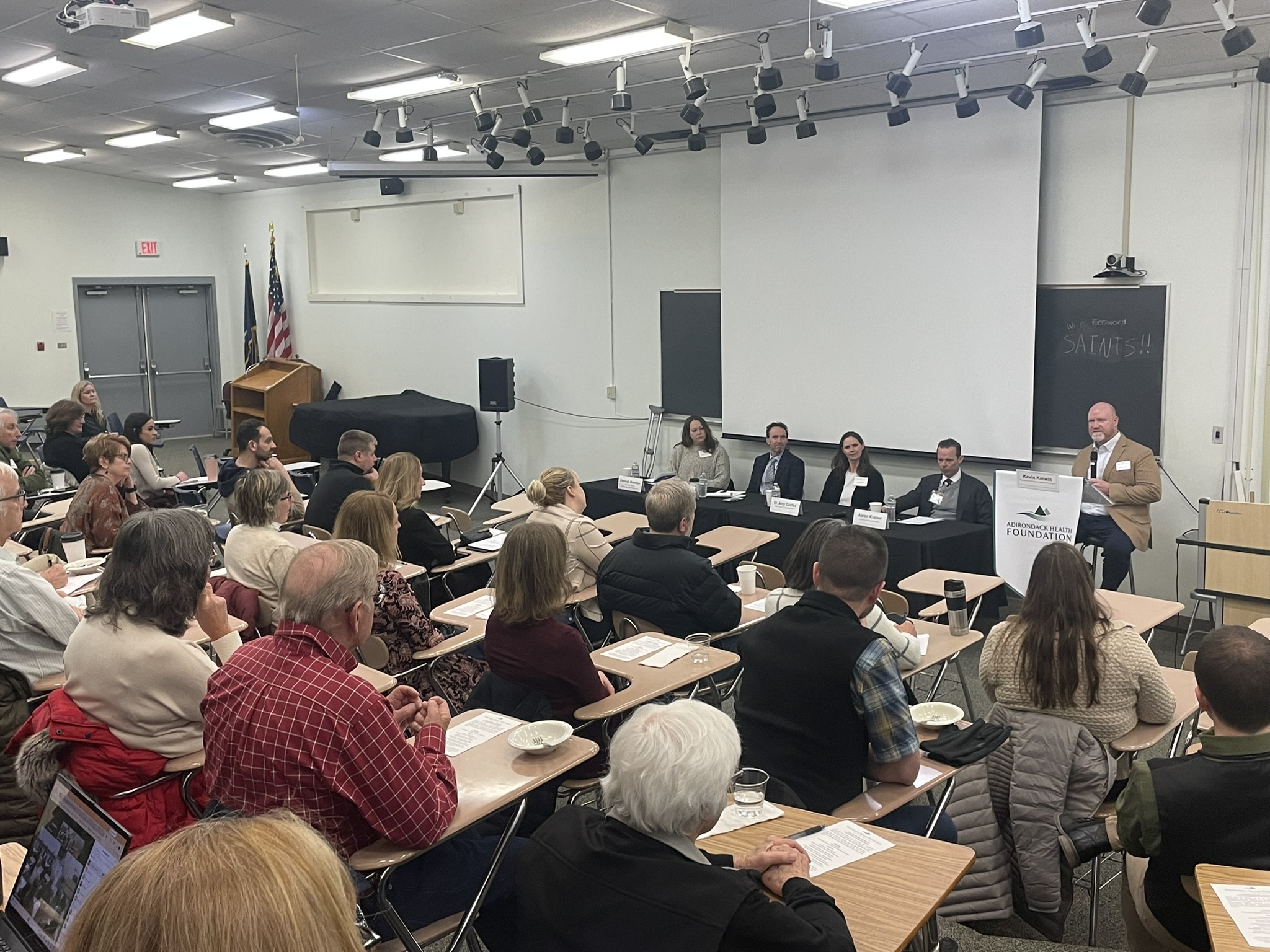 A person speaks at a podium in a lecture hall as a group of people in seats listen
