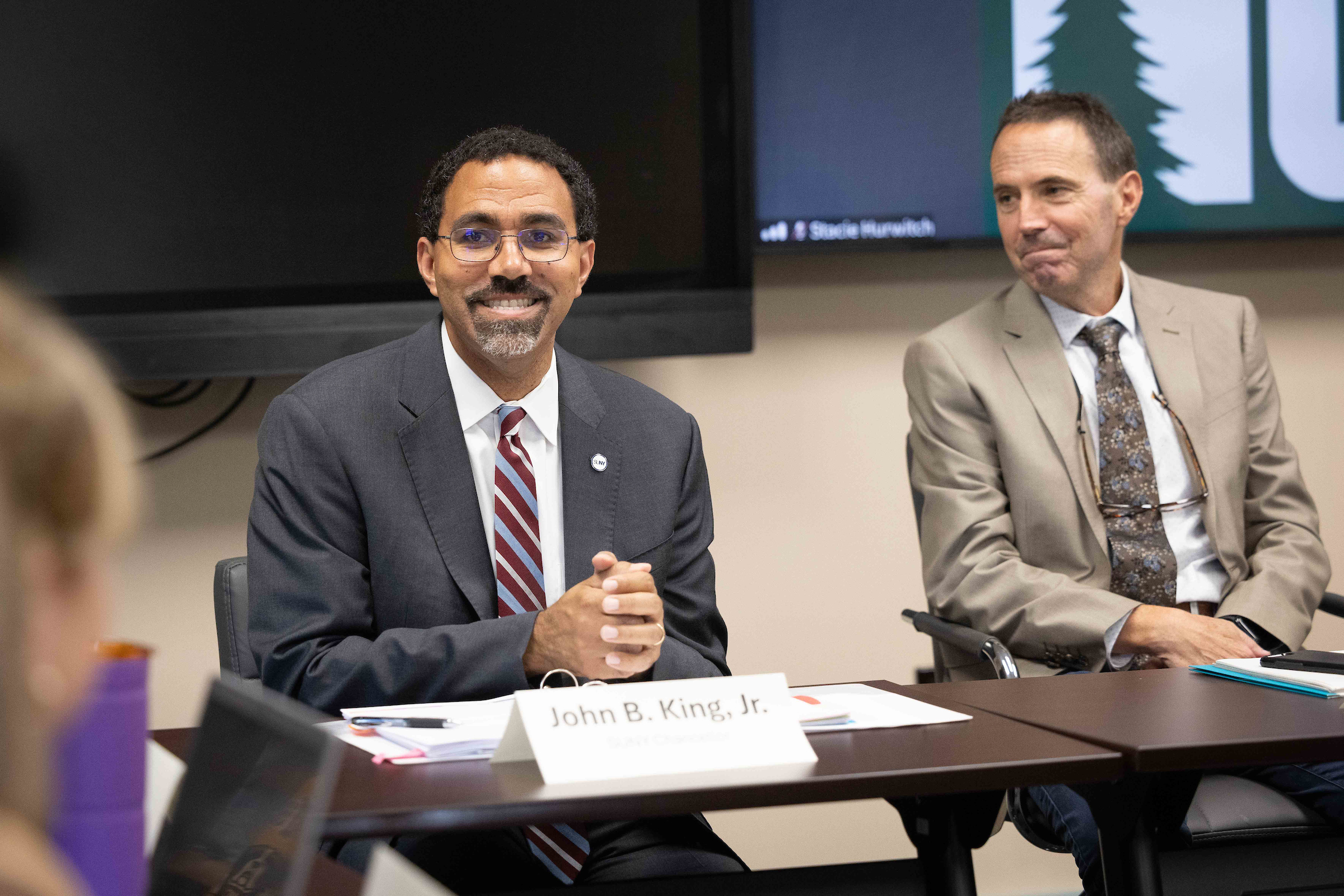 SUNY Chancellor John King smiles as he sits at a table next to NCCC President Joe Keegan