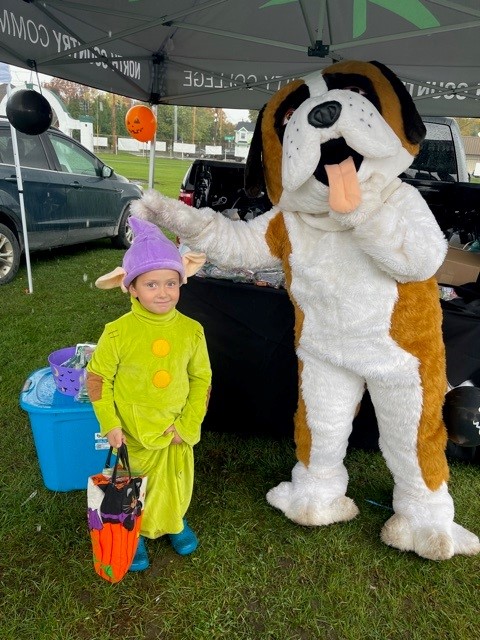 A child in costume stands next to the NCCC mascot, Bernie the St. Bernard.