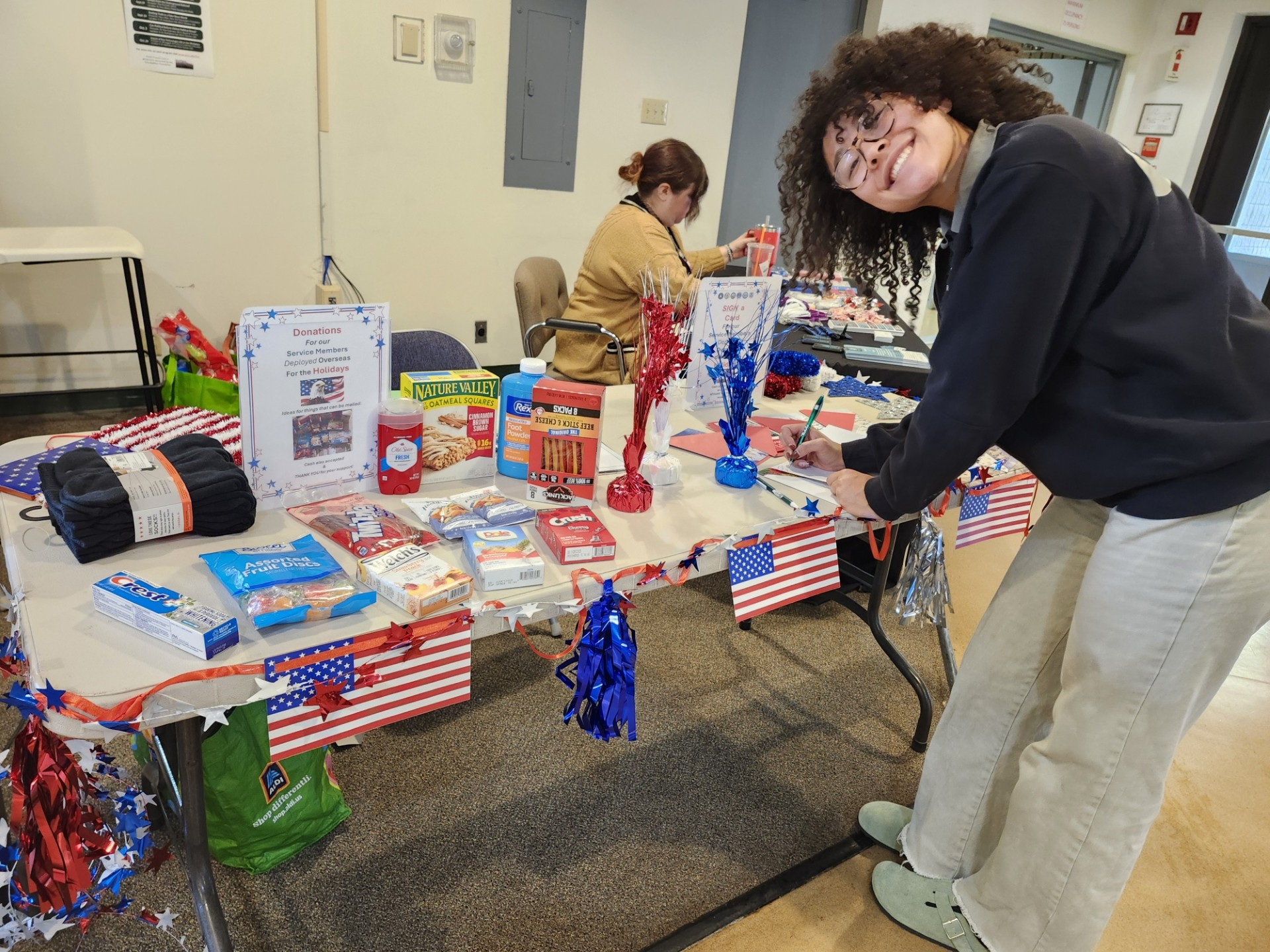 A student smiles at the camera as she signs a card at a table 