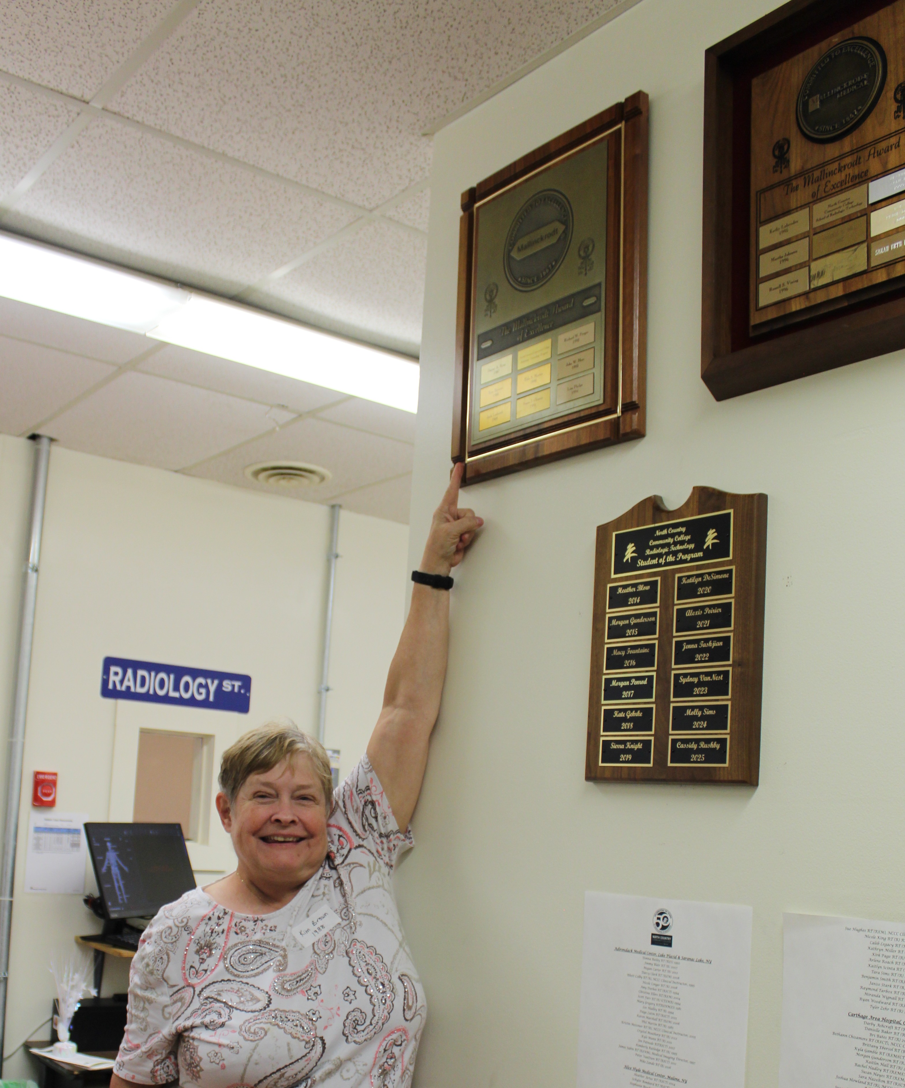 A graduate of NCCC's Radiologic Technology program points to her name on a plaque