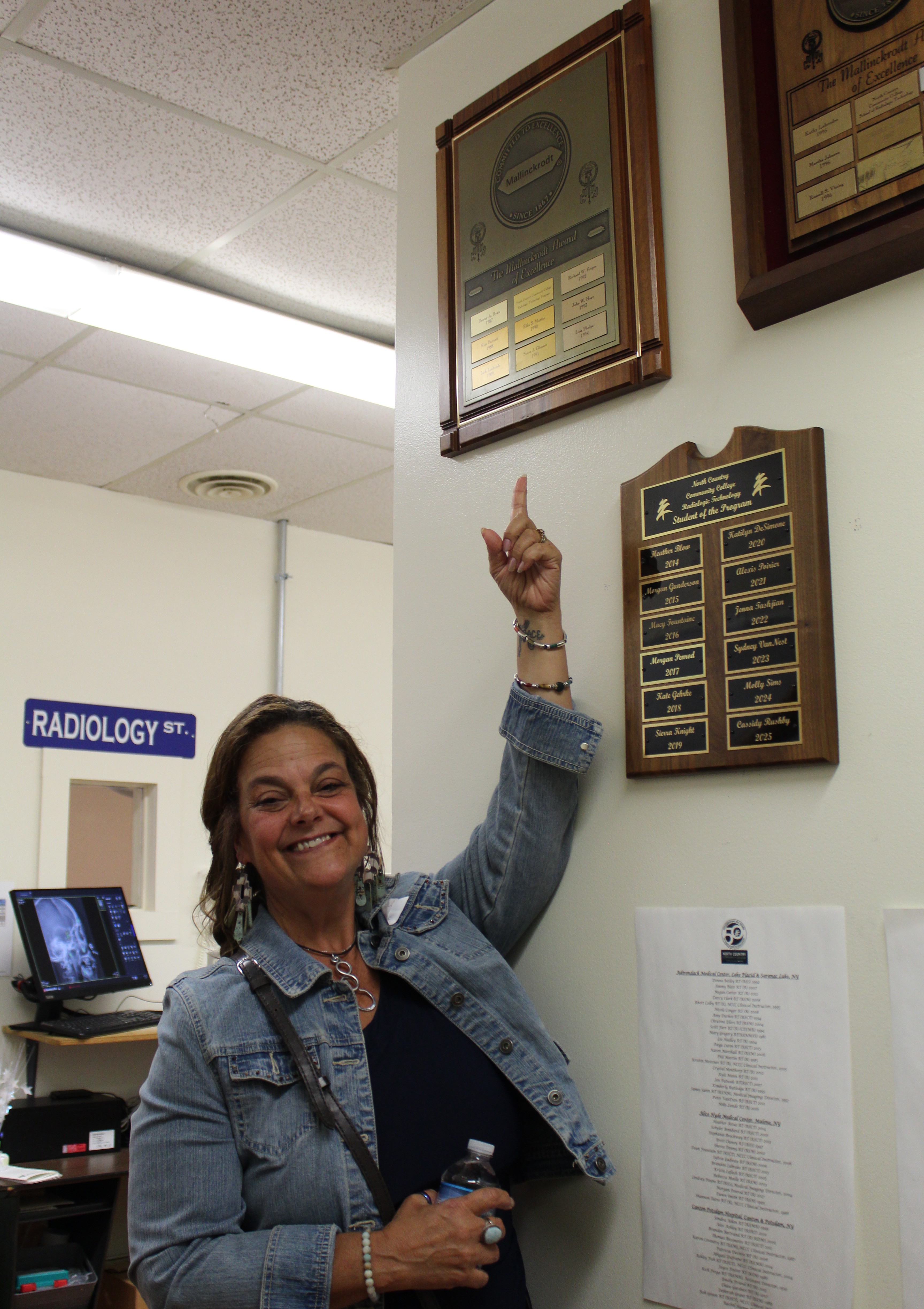 A graduate of NCCC's Radiologic Technology program points to her name on a plaque