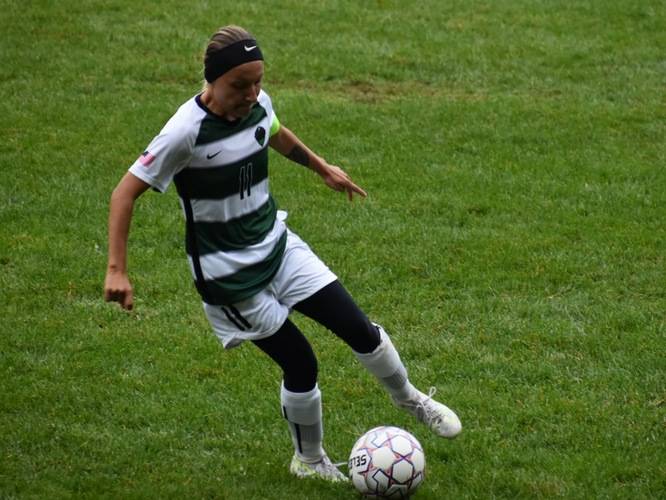 A soccer player with the ball at her feet on a field.