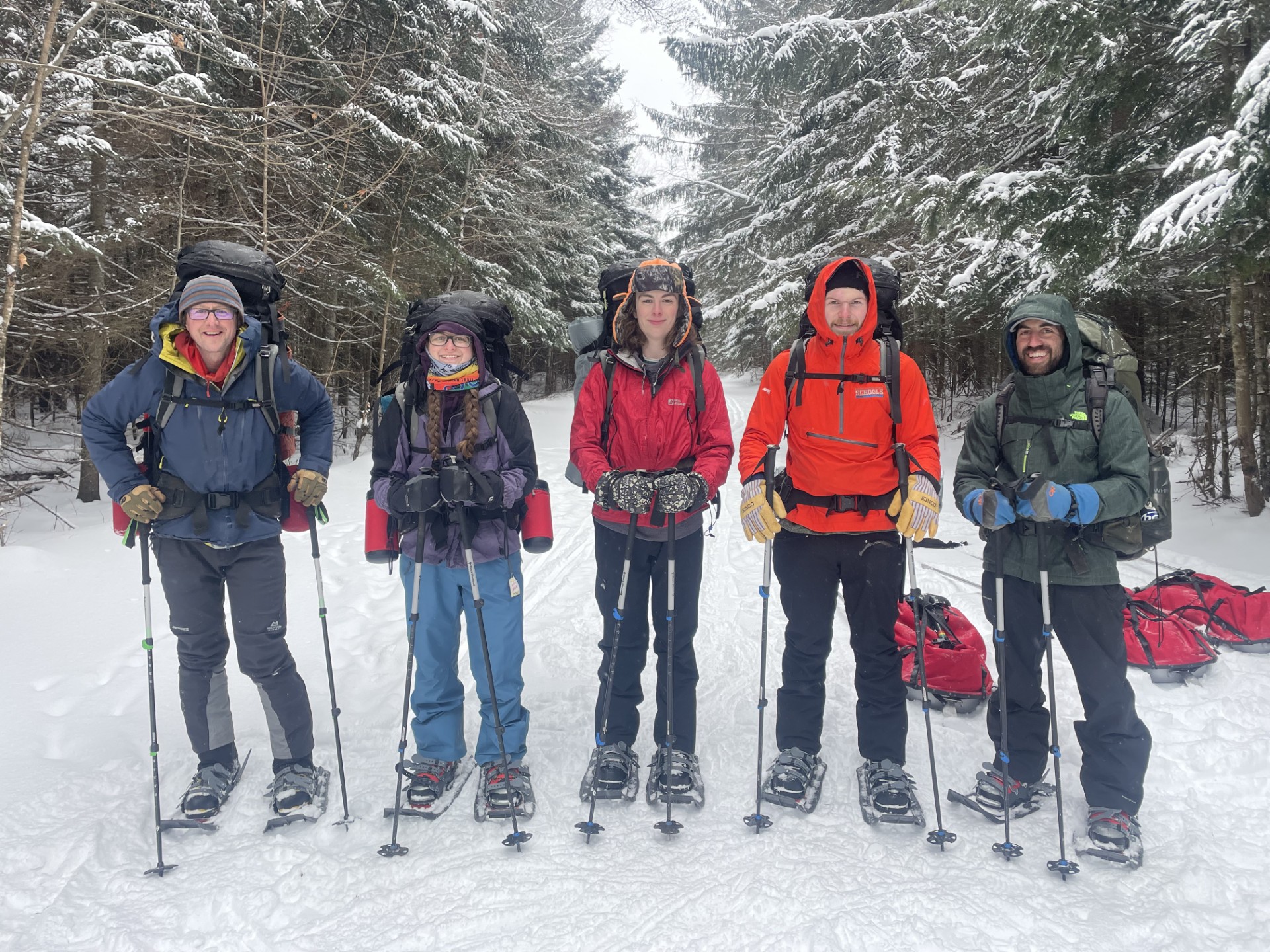 A group of college students and instructors stand against a backdrop of snow and trees